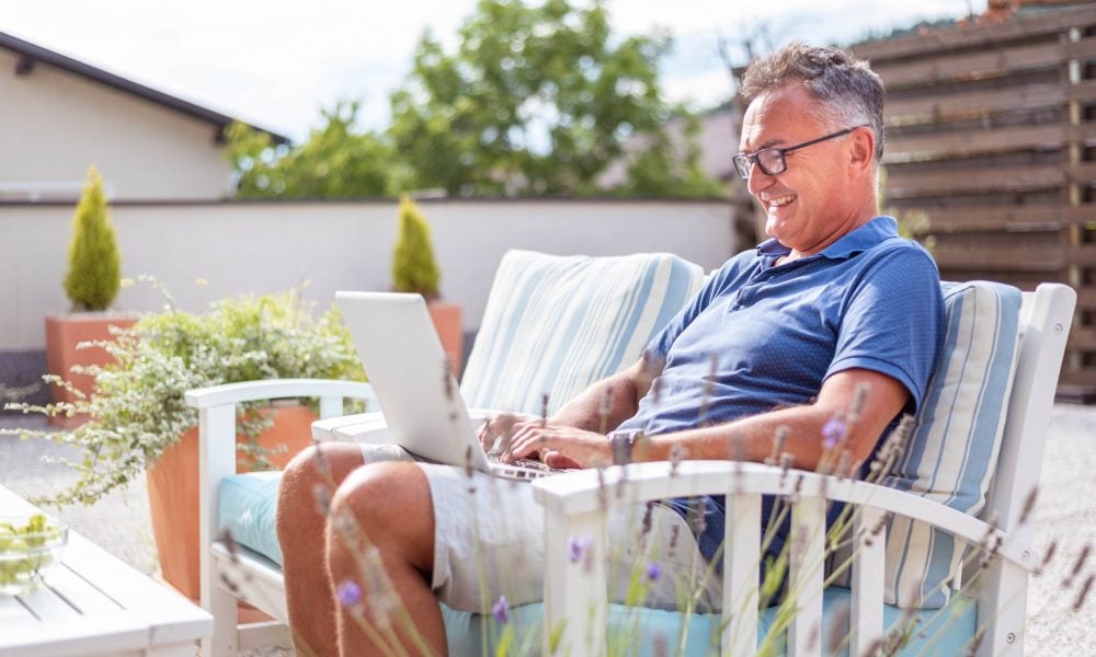 A man works on his laptop in his patio garden.
